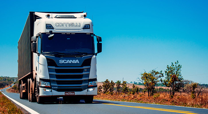 A lorry driving on an asphalt road with blue sky in the background.