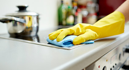 A hand with a yellow glove wipes the stove with a rag.