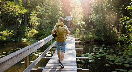 Henkilö kävelee sillalla kesäisessä maisemassa.