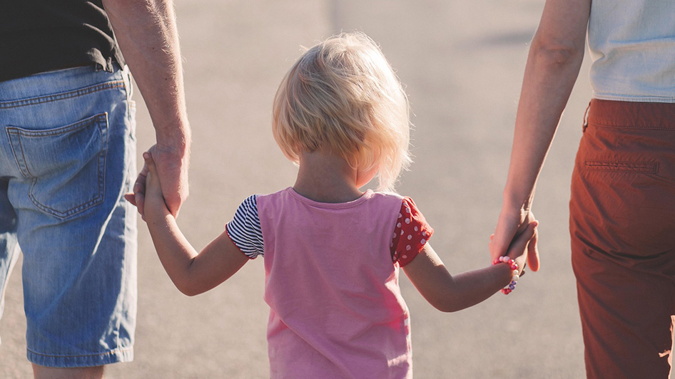 A child is walking outdoors holding hands with two adults.