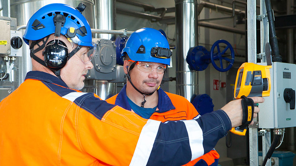 Kaksi kypäräpäistä työntekijää tutkii laitetta. Kuva: Anu Pynnönen.