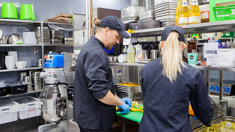 Kaksi työntekijää valmistaa ruokaa keittiössä. Kuva: Anu Pynnönen.
